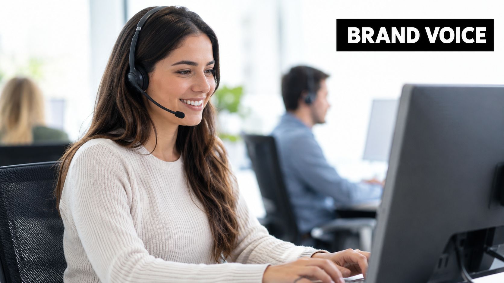 A smiling customer service representative with a headset working at a computer in an office environment.