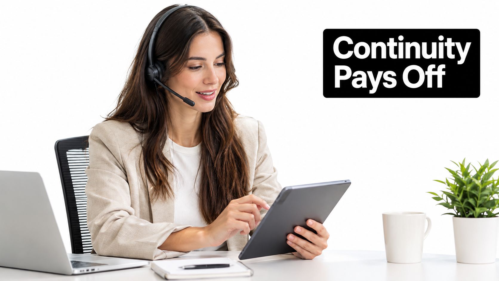 A professional customer service representative wearing a headset uses a tablet while working at an office desk.
